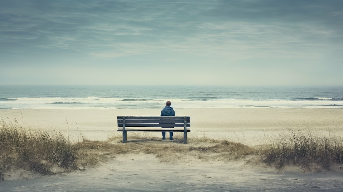 young man sitting on a bench on the beach looking out over the waves